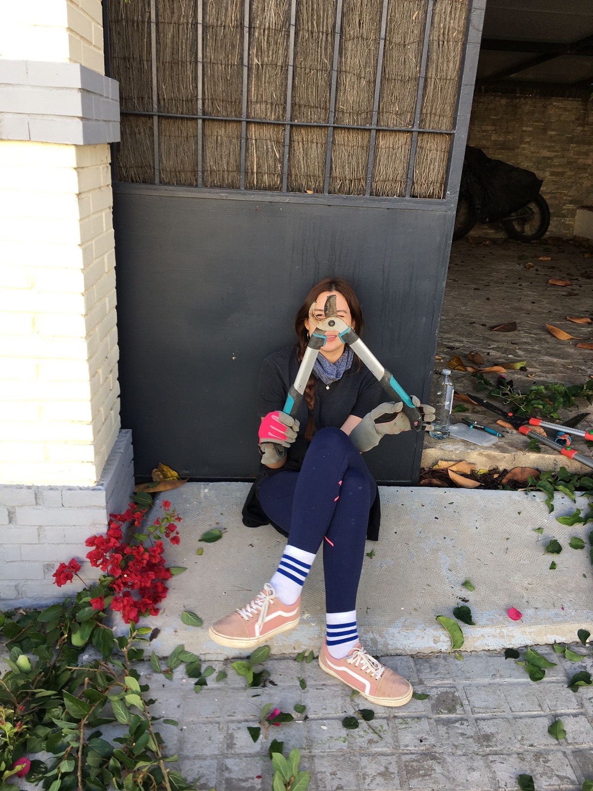 Una jardinera sonriente posa con tijeras de podar mientras se sienta en un banco rodeada de herramientas y plantas recién cuidadas