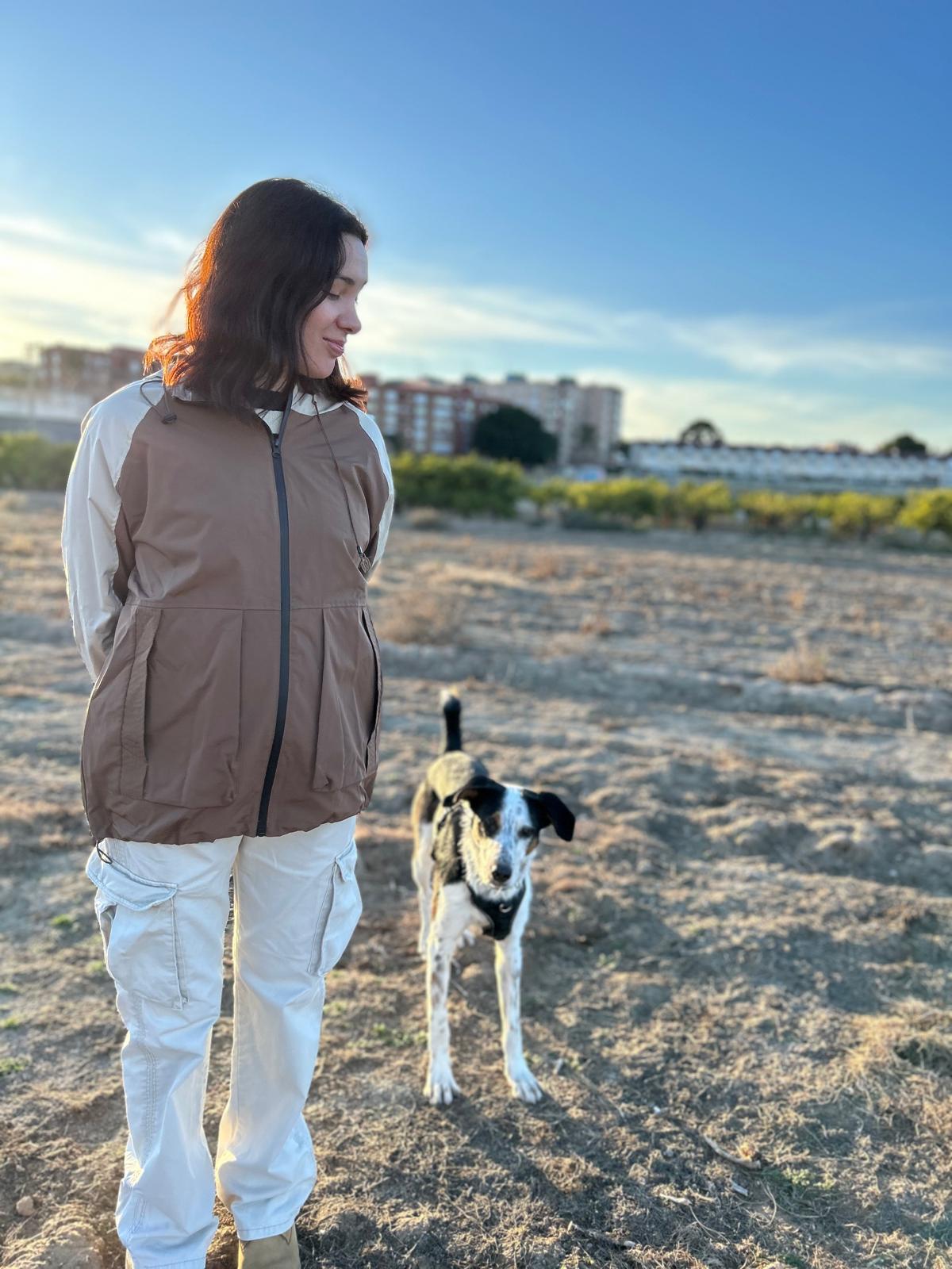 Mujer caminando junto a su perro en un campo abierto bajo un cielo despejado.